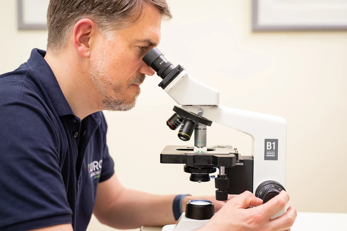 Ein Urologe der CUROS sitzt an einem Mikroskop und untersucht eine Probe.